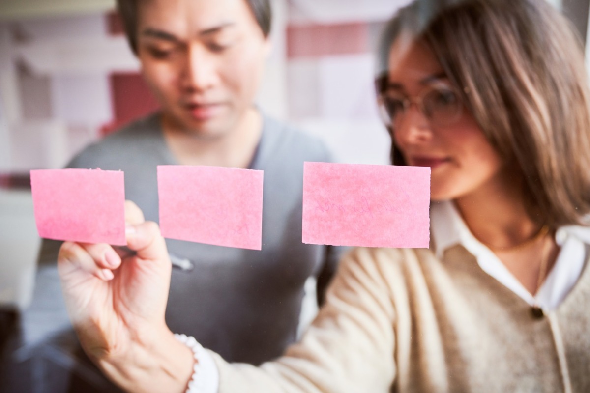 Mitarbeiterin beschriftet Post its an einer Glastafel