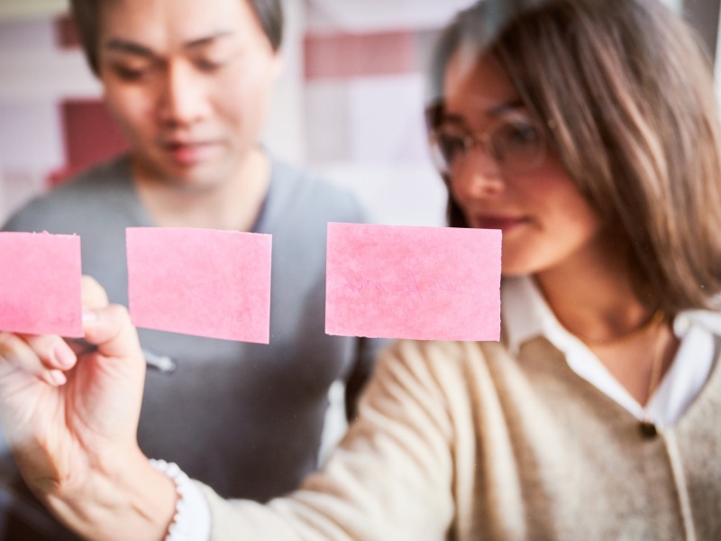 Mitarbeiterin beschriftet Post its an einer Glastafel