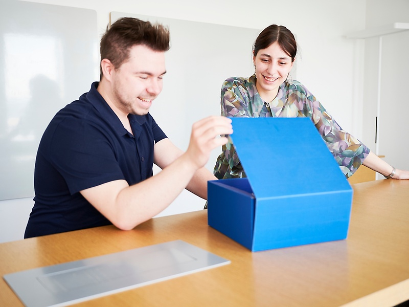 Mitarbeitende an einem Schreibtsich öffenen ein blaues Paket