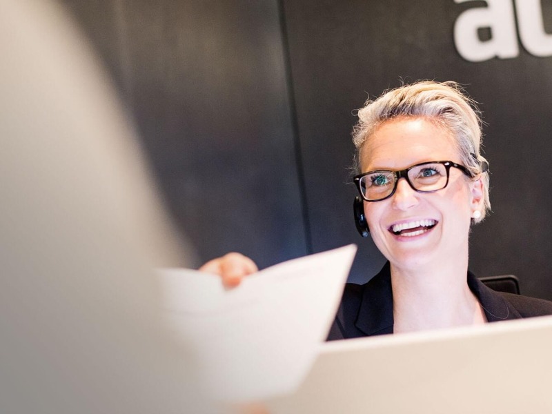 Smiling blonde woman with short hair at reception hands over a document 