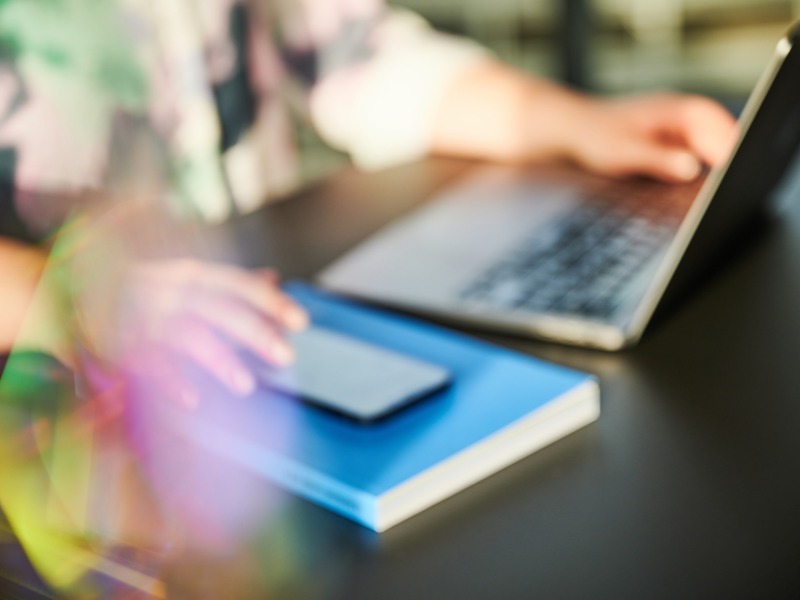 Foto von Person mit einer Hand auf der Laptoptastatur und einer am Smartphone