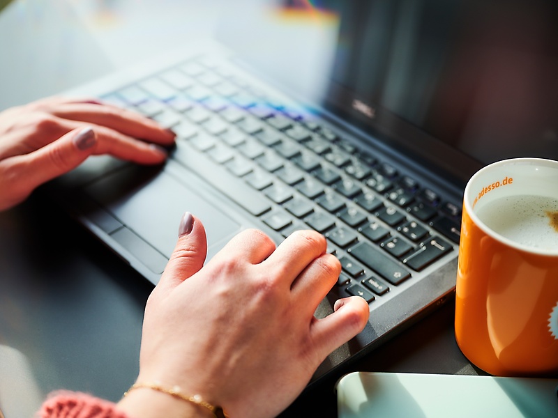 someone is typing on a laptop an a cup of coffee is standing next to the laptop