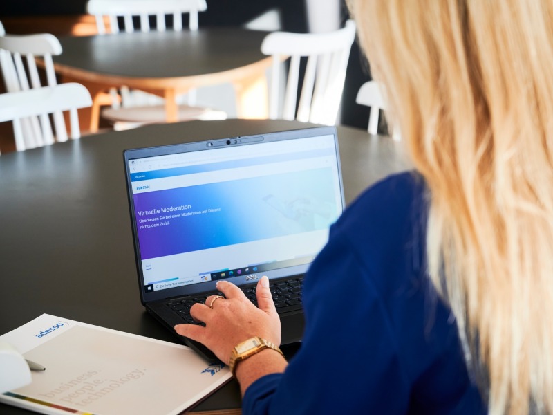 Blonde Frau sitzt am Tisch und tippt auf einem Notebook